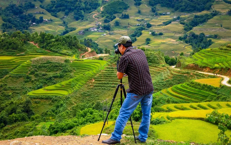 A photographer with a tripod camera captures the terraced rice fields cascading down the mountains near Sapa. A photographer with a tripod camera captures the terraced rice fields cascading down the mountains near Sapa.