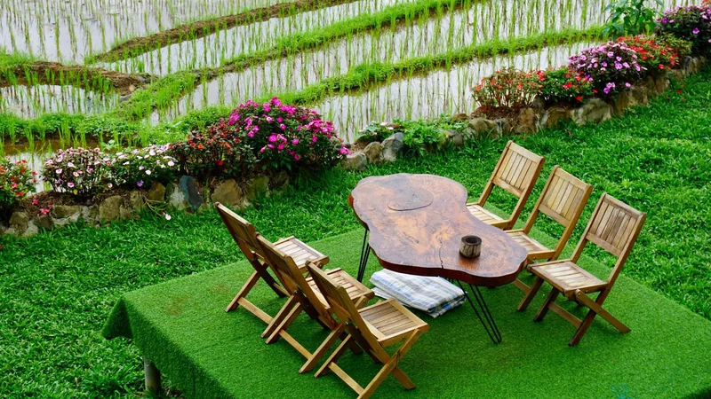 A wooden table and chairs sit on a lawn beside terraced rice paddies and flowers in Pu Luong. A wooden table and chairs sit on a lawn beside terraced rice paddies and flowers in Pu Luong.