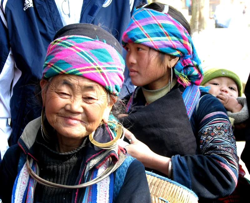 A Black Hmong grandmother, mother, and baby in colorful plaid headscarves and silver jewelry near Sapa. A Black Hmong grandmother, mother, and baby in colorful plaid headscarves and silver jewelry near Sapa.