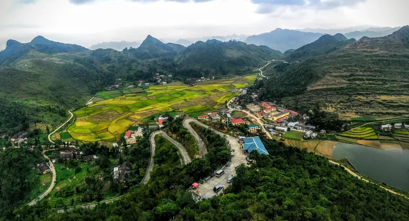 Winding roads curve through a green valley of terraced rice fields surrounded by mountains near Dong Van, Ha Giang.