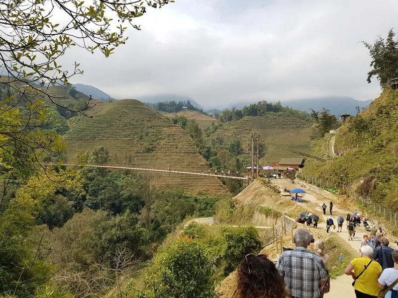 Tourists walk a mountain trail past terraced hills and a suspension bridge near Sapa's Muong Hoa valley. Tourists walk a mountain trail past terraced hills and a suspension bridge near Sapa's Muong Hoa valley.