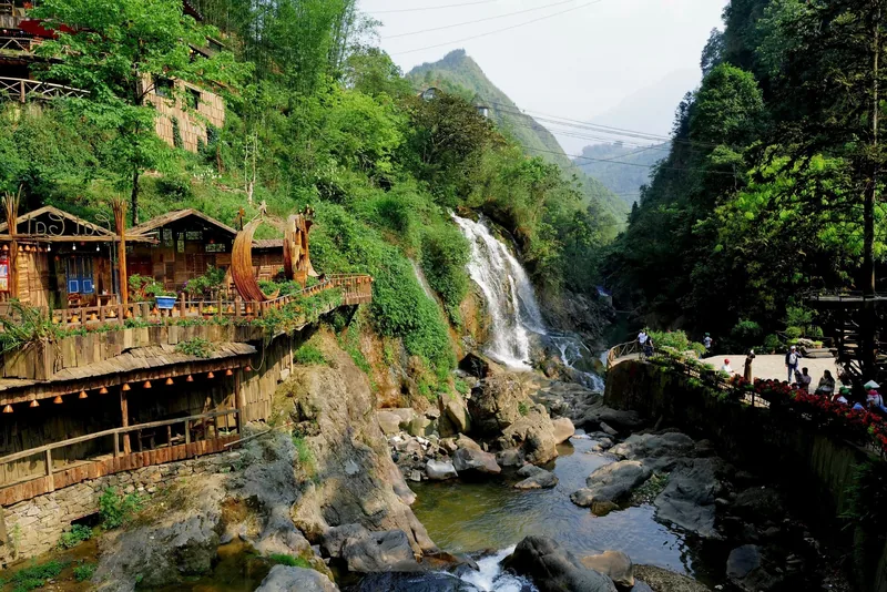 A wooden waterwheel and cafe overlook a waterfall cascading through rocks in Cat Cat Village. A wooden waterwheel and cafe overlook a waterfall cascading through rocks in Cat Cat Village.