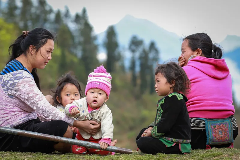 Hmong mothers and children sit together on grass with misty Sapa mountains in the background. Hmong mothers and children sit together on grass with misty Sapa mountains in the background.
