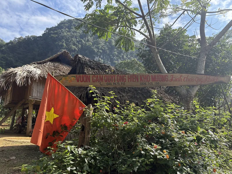 A thatched-roof stilt house with a Vietnamese flag and a hand-painted sign stands amid greenery in Pu Luong. A thatched-roof stilt house with a Vietnamese flag and a hand-painted sign stands amid greenery in Pu Luong.