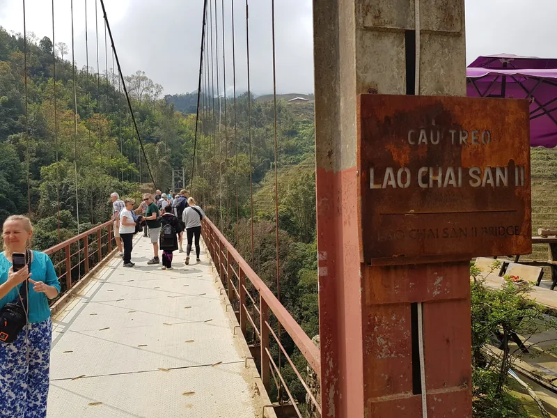 Tourists cross the Lao Chai San II suspension bridge over a green valley near Sapa.