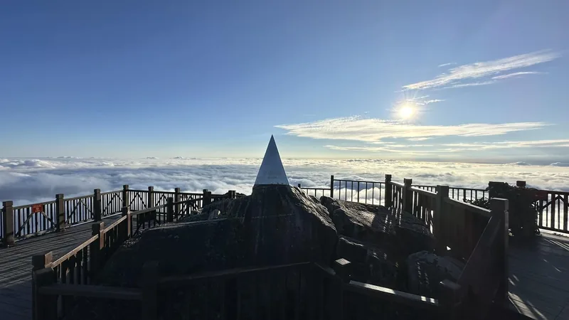 A metal peak marker on a wooden viewing deck rises above a sea of clouds atop Fansipan mountain. A metal peak marker on a wooden viewing deck rises above a sea of clouds atop Fansipan mountain.