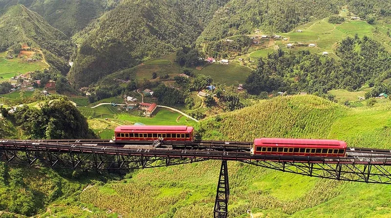 A red funicular train crosses a high trestle bridge over the green Muong Hoa valley near Fansipan. A red funicular train crosses a high trestle bridge over the green Muong Hoa valley near Fansipan.