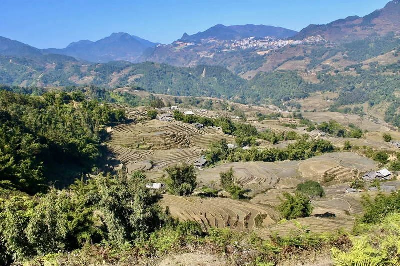 Terraced rice fields spread across a valley below Sapa town, framed by mountain ridges under a clear sky. Terraced rice fields spread across a valley below Sapa town, framed by mountain ridges under a clear sky.