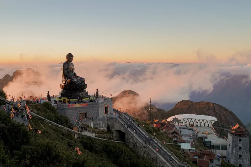 A giant bronze Buddha statue crowns Fansipan's summit above a sea of clouds at sunset. A giant bronze Buddha statue crowns Fansipan's summit above a sea of clouds at sunset.